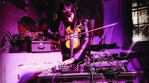 Anju Singh playing a violin while turning a knob on her pedalboard